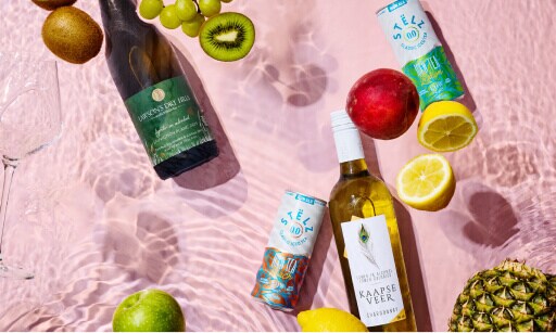 Laag in alcohol: 2 wijnen en 2 blikjes die weinig of geen alcohol bevatten op een roze achtergrond met citroenen, kiwi's, appels en ananas